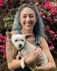 a person with blue hair smiles with her dog.