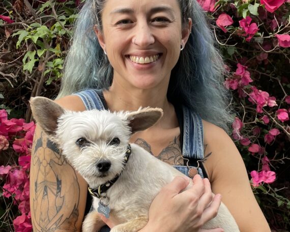 a person with blue hair smiles with her dog.