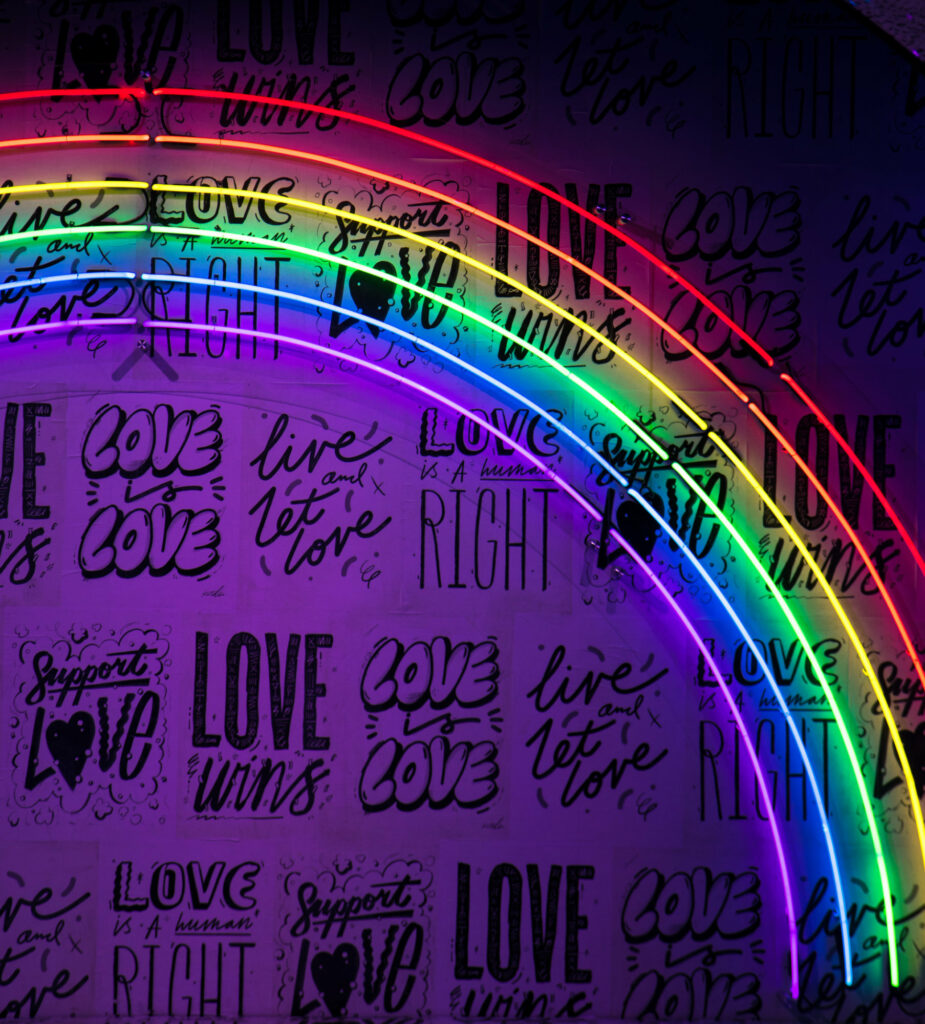 A neon rainbow decorates a wall with various "love is love" signage.